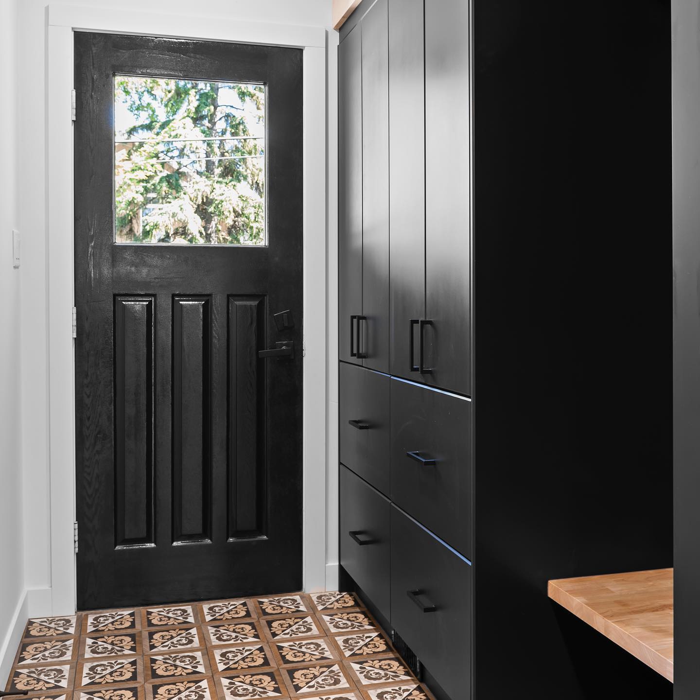 Finished entryway with patterned tile, black door, and built-in cabinetry