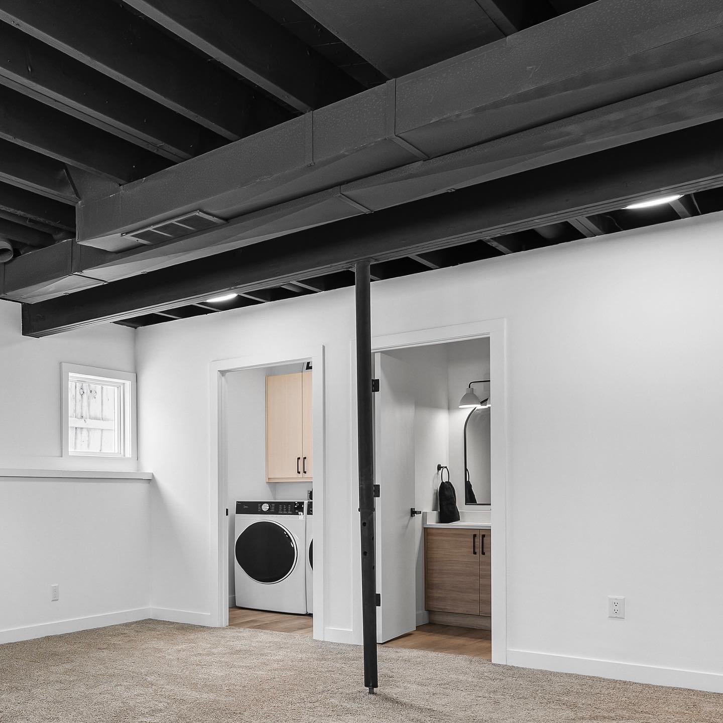 Finished basement with exposed ceiling beams and bright neutral walls